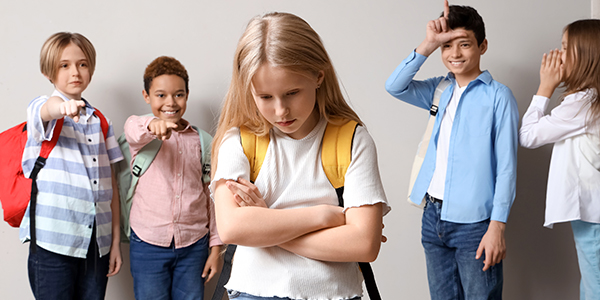 Criança de cabeça baixa sofrendo bullying e colegas atrás dela apontando o dedo. 